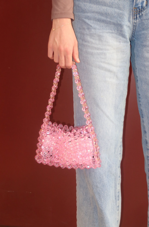 Person holding a pink beaded handbag against a red background